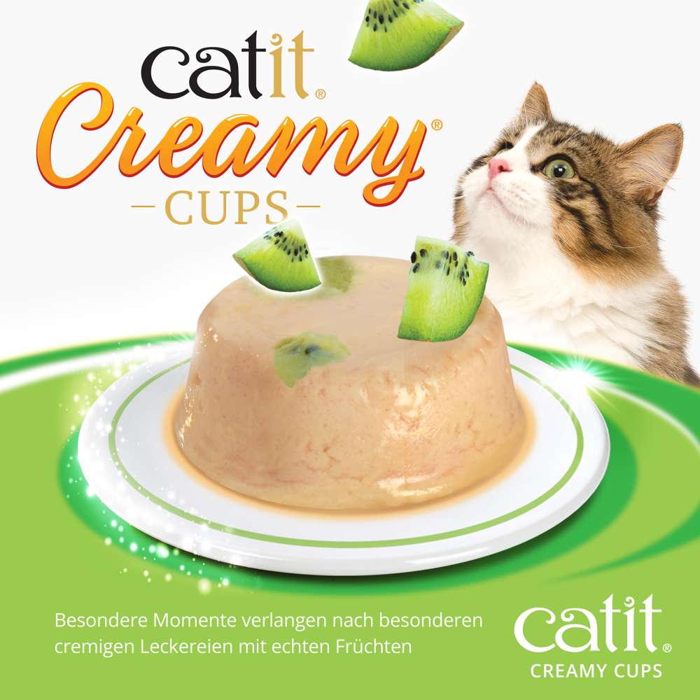 Die "Catit Creamy Cups" der Sorte "Huhn & Kiwi" in Nah-Ansicht. Eine Katze schaut neugierig.