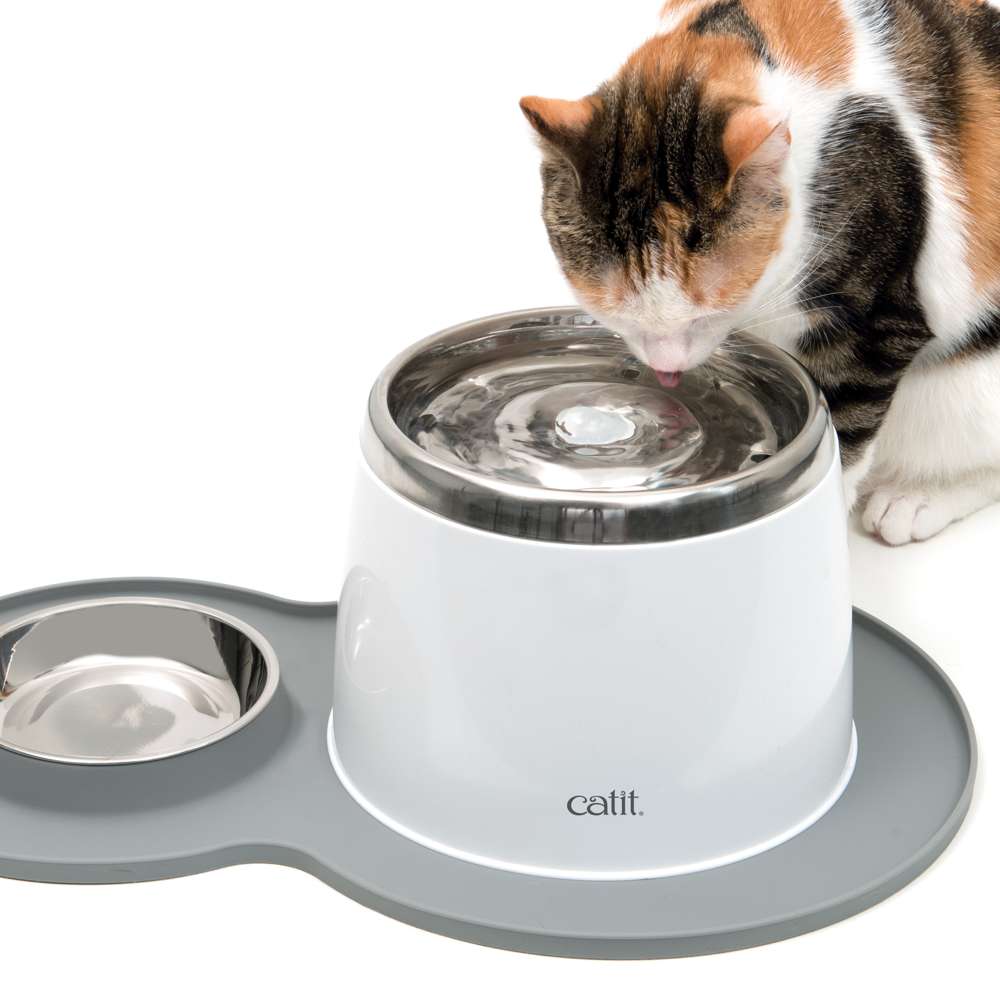Graue Catit Erdnuss-Unterlegmatte mit Napf und Trinkbrunnen. Katze trinkt.