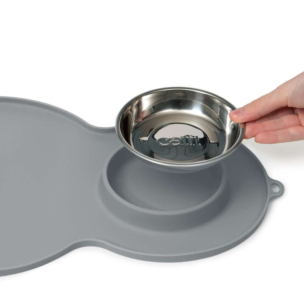 Eine Hand stellt einen Futternapf auf die Unterlage.